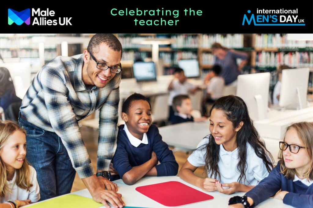 A young black male teacher leaning on a table surrounded by young students, all of them are smiling.