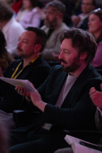 A close up of two male members of the audience at the National Allyship Summit smiling and clapping.